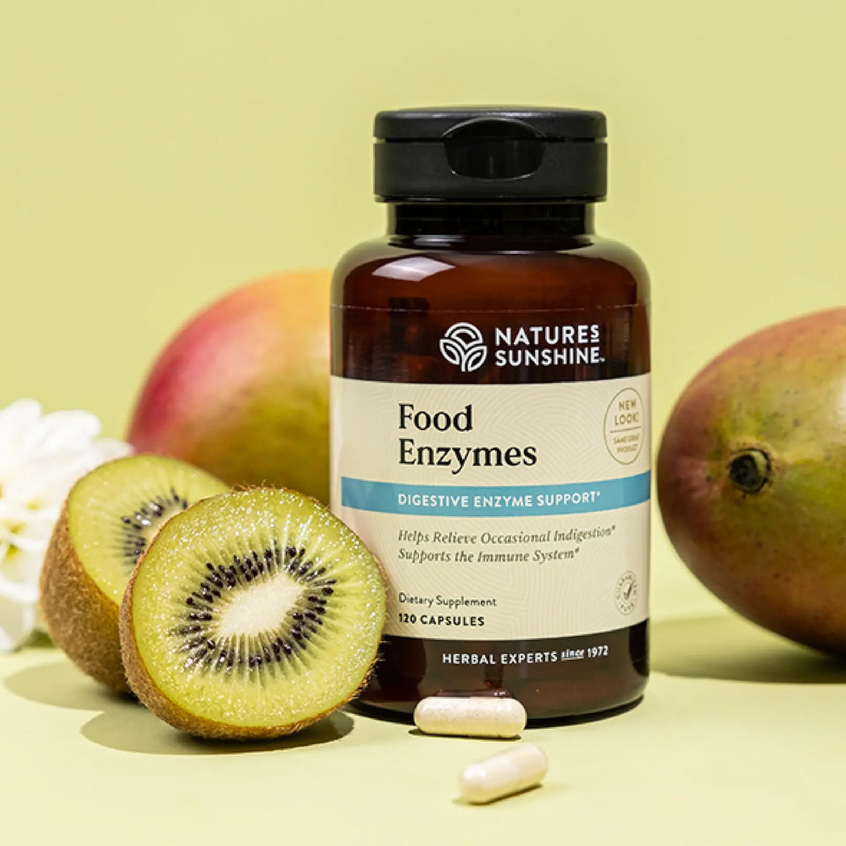 A bottle of Nature's Sunshine Food Enzymes dietary supplement, styled with kiwi slices and mangoes on a pale yellow-green background.