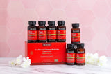 A set of Nature's Organics Traditional Chinese Medicine supplement bottles and a red gift box arranged on a marble surface with white flowers, against a pink hexagonal background.