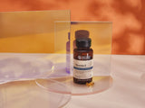 A bottle of Nature's Bounty Vitamin E dietary supplement with a black cap and amber glass bottle, displayed on a clear acrylic stand with a small capsule in front, set against a warm orange and yellow gradient background.