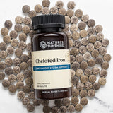 Nature's Sunshine Chelated Iron supplement bottle surrounded by iron supplements on a marble surface.