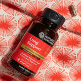A bottle of Nature's Sunshine Lung Support dietary supplement capsules, placed on a red and white patterned fabric background with a single capsule nearby.