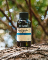 A bottle of Nature's Sunshine Liquid Methyl Vitamin B3 Complete placed on a textured tree trunk with a blurred forest background.