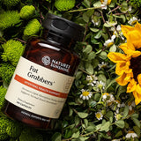 Nature's Sunshine Fat Grabbers supplement bottle on a natural background with greenery and flowers.