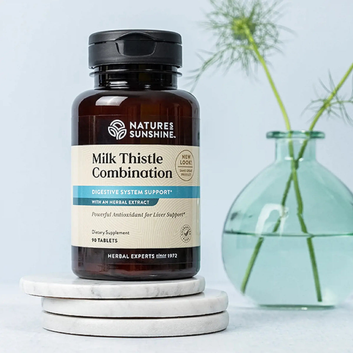 A bottle of Nature's Sunshine Milk Thistle Combination dietary supplement, styled on stacked white marble coasters with a light blue background and a green glass vase in the background.