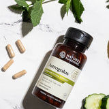 A bottle of Nature's Sunshine Astragalus immune system support dietary supplement capsules, styled on a white marble surface with green leaves, cucumber slices, and loose capsules.