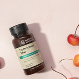 A bottle of Nature's Sunshine Nattozimes Plus dietary supplement capsules, styled on a light pink background with decorative cherries.