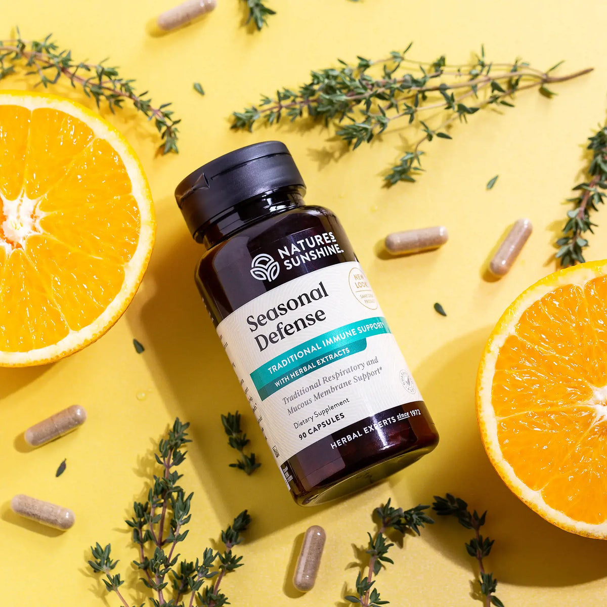 A bottle of Nature's Sunshine Seasonal Defense herbal supplement capsules, styled in a flat-lay on a bright yellow background with orange slices, fresh thyme, and scattered capsules.