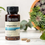 Nature's Sunshine AdaptaMax supplement bottle on a white surface with plants in the background