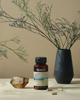 A bottle of Nature's Recommendations Enviro-Detox dietary supplement capsules, styled on a beige surface with a dark ceramic vase of dried stems, a crystal, and loose capsules.