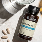 Nature's Sunshine Glucosamine Joint Support supplement bottle on a textured light gray surface with scattered capsules and a glass in the background.