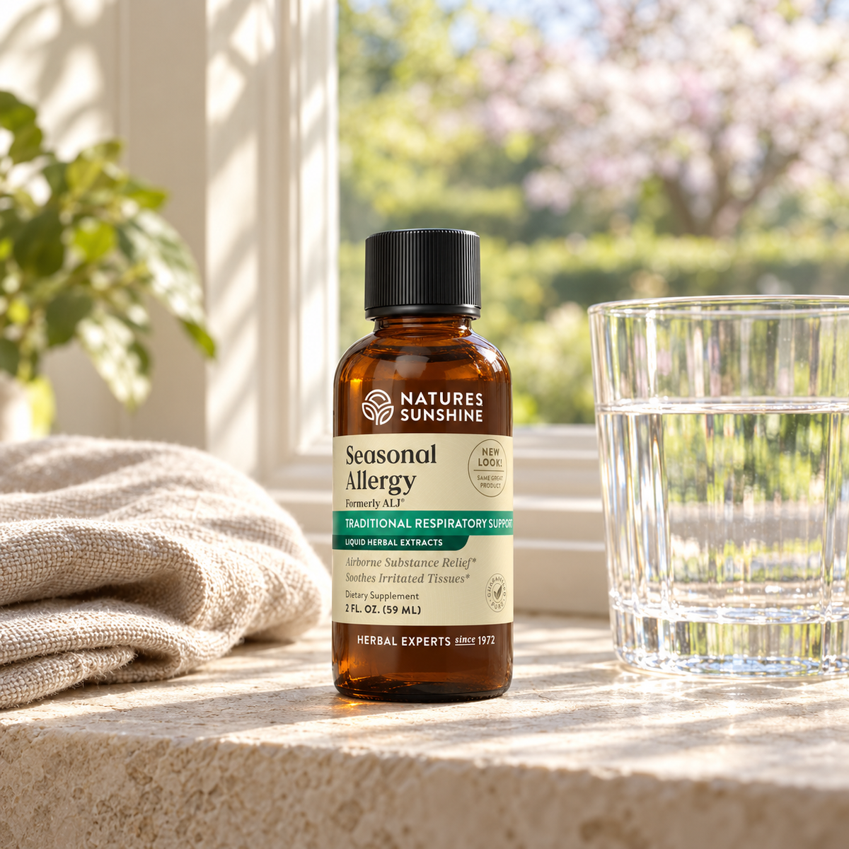 A bottle of Nature's Sunshine Seasonal Allergy Relief syrup placed on a stone surface next to a glass of water, with a beige cloth and a blurred outdoor garden background.