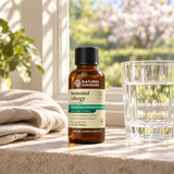 A bottle of Nature's Sunshine Seasonal Allergy Relief syrup placed on a stone surface next to a glass of water, with a beige cloth and a blurred outdoor garden background.