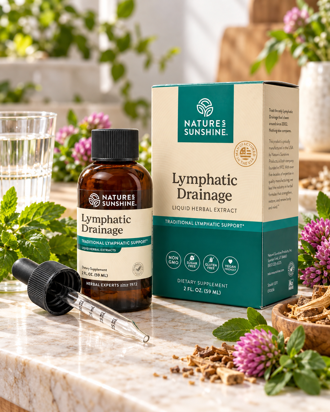 Nature's Sunshine Lymphatic Drainage herbal supplement shown with its amber glass bottle, black dropper, and cream-and-teal product box on a marble surface, surrounded by flowers, greenery, and a glass of water.