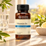 A bottle of Nature's Sunshine Vitamin D3 dietary supplement, set on a stone surface with a glass of water and lemon slices in a bright, sunny outdoor setting.