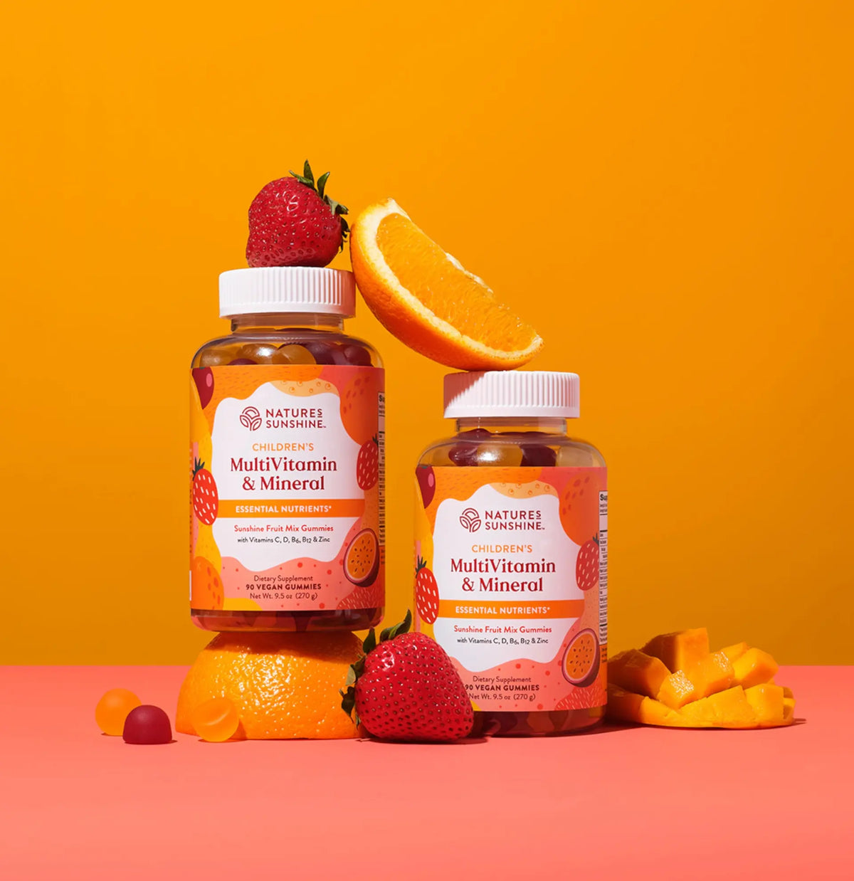 Two Nature's Sunshine MultiVitamin & Minerol bottles styled with fresh fruit on a pink and orange studio background.