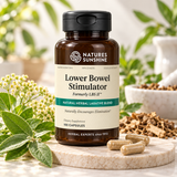 A bottle of Nature's Sunshine Lower Bowel Stimulator dietary supplement, styled on a marble tray with loose capsules and herbal ingredients against a soft-focus background of green leaves.